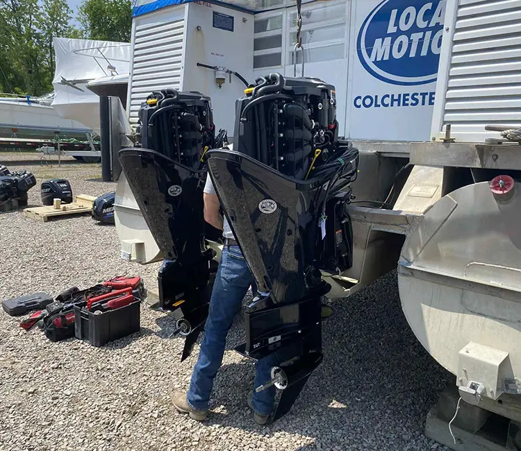 Technician servicing twin outboard motors during on-location boat repair in Vermont